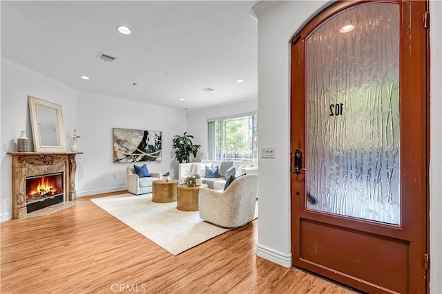 living room with a premium fireplace, ornamental molding, and light hardwood / wood-style flooring