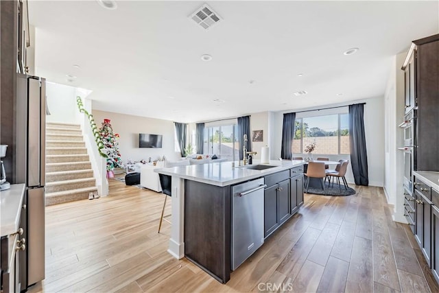 kitchen featuring dark brown cabinets, stainless steel appliances, light hardwood / wood-style floors, and a kitchen island with sink