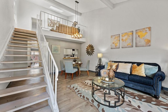 living room featuring beam ceiling, wood-type flooring, a towering ceiling, and an inviting chandelier