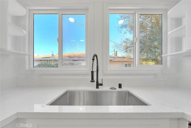 room details featuring white cabinets, light stone counters, and sink