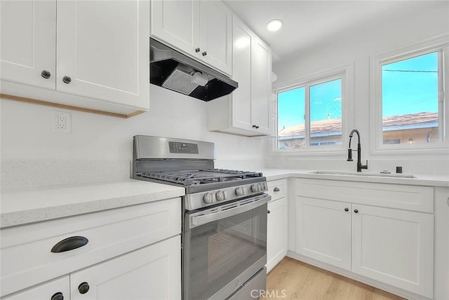 kitchen with light stone countertops, light wood-type flooring, sink, white cabinetry, and stainless steel range with gas stovetop