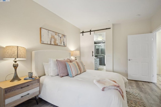 bedroom featuring hardwood / wood-style floors, ensuite bath, and a barn door