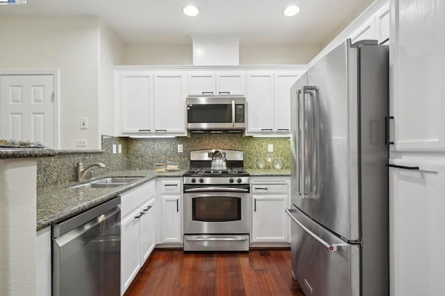 kitchen featuring appliances with stainless steel finishes, backsplash, dark stone counters, white cabinets, and sink