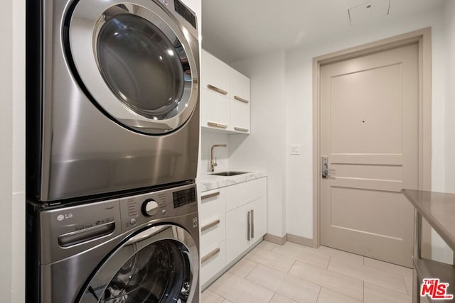 clothes washing area with stacked washing maching and dryer, light tile patterned flooring, sink, and cabinets