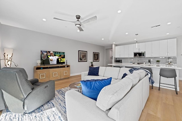 living room with ceiling fan, sink, and light hardwood / wood-style flooring