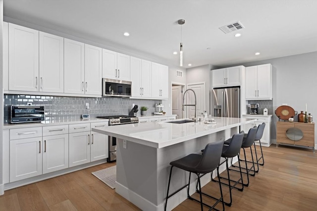 kitchen featuring a breakfast bar area, an island with sink, white cabinets, and appliances with stainless steel finishes