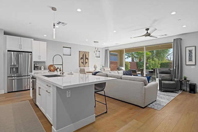 kitchen with stainless steel appliances, white cabinetry, sink, and a center island with sink