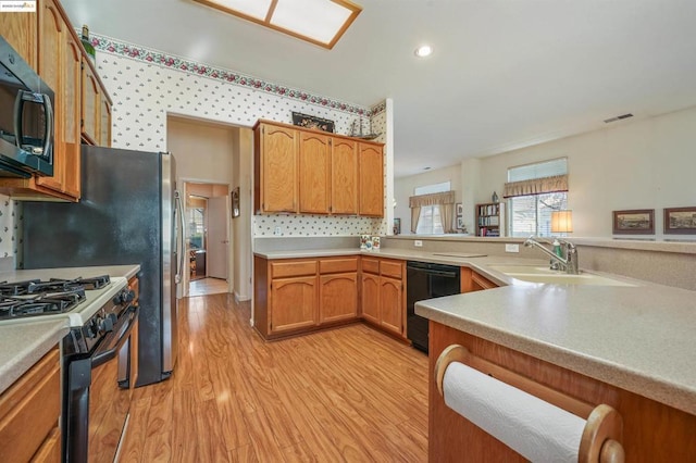 kitchen featuring range with gas cooktop, kitchen peninsula, sink, black dishwasher, and light hardwood / wood-style flooring