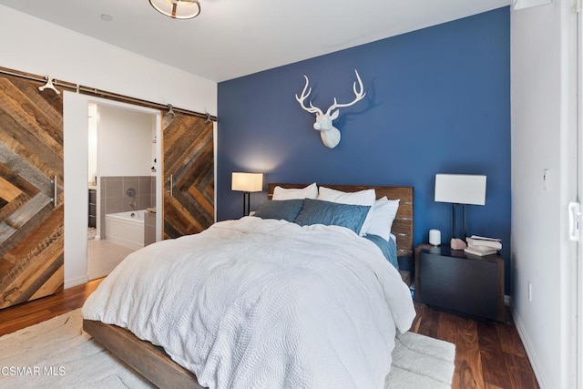 bedroom featuring wood-type flooring, connected bathroom, and a barn door