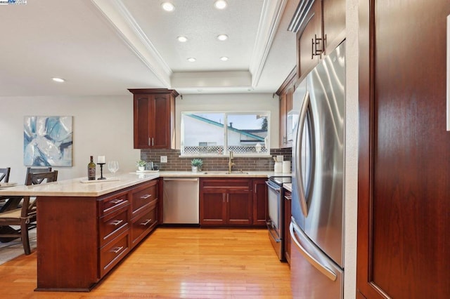 kitchen featuring sink, light hardwood / wood-style flooring, a tray ceiling, kitchen peninsula, and stainless steel appliances