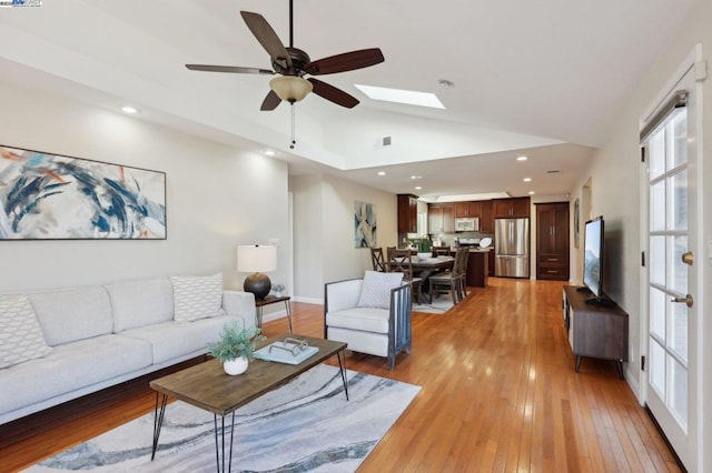 living room with a skylight, high vaulted ceiling, ceiling fan, and light hardwood / wood-style flooring