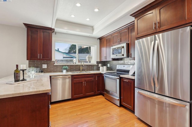 kitchen featuring sink, stainless steel appliances, tasteful backsplash, a tray ceiling, and light hardwood / wood-style floors