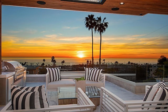 patio terrace at dusk with area for grilling, a grill, and a water view