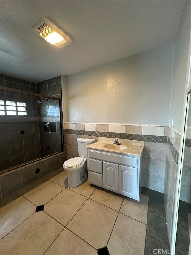 bathroom with toilet, tile walls, vanity, a shower with door, and tile patterned flooring