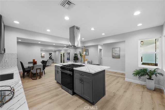 kitchen featuring gray cabinetry, light stone countertops, light hardwood / wood-style floors, island exhaust hood, and stainless steel range with gas cooktop