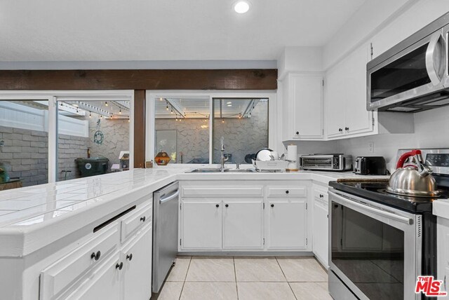 kitchen with appliances with stainless steel finishes, white cabinetry, sink, kitchen peninsula, and light tile patterned floors