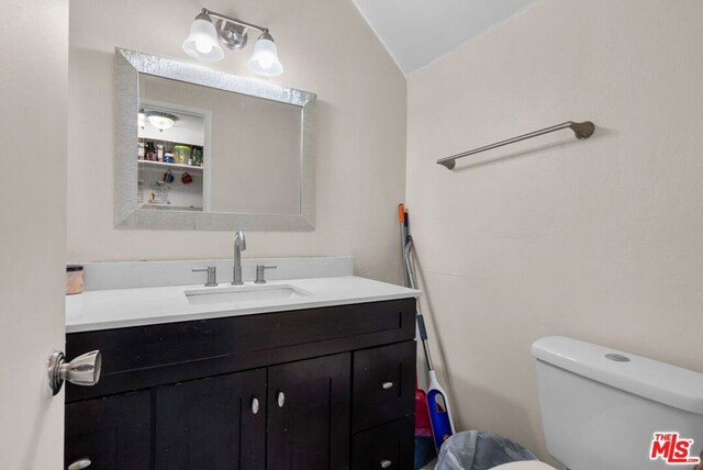 bathroom featuring toilet, vanity, and lofted ceiling