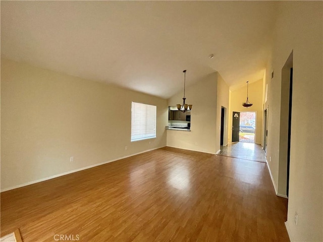 empty room with high vaulted ceiling, a healthy amount of sunlight, a chandelier, and hardwood / wood-style flooring