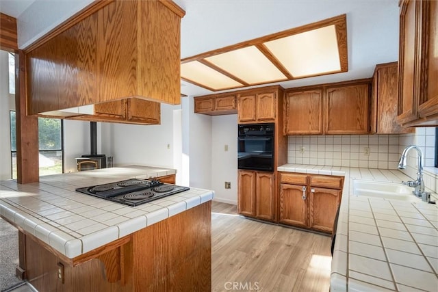 kitchen featuring a wood stove, kitchen peninsula, black appliances, and tile counters