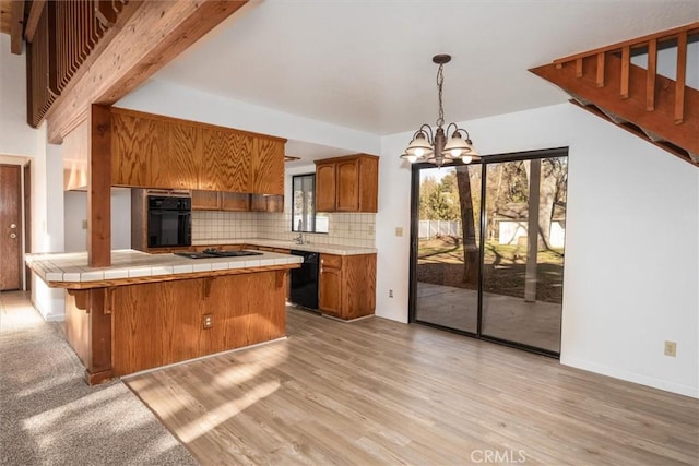 kitchen featuring tasteful backsplash, a notable chandelier, light hardwood / wood-style floors, black appliances, and tile counters