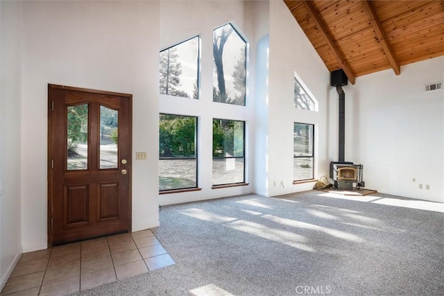 unfurnished living room featuring wood ceiling, beamed ceiling, a wood stove, light tile patterned flooring, and high vaulted ceiling