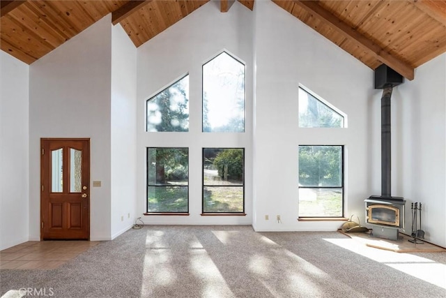 unfurnished living room featuring high vaulted ceiling, beamed ceiling, a wood stove, and wooden ceiling