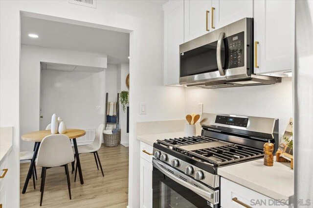 kitchen with appliances with stainless steel finishes, light hardwood / wood-style floors, and white cabinetry