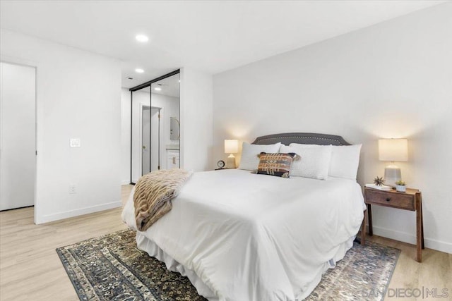 bedroom featuring ensuite bathroom, a closet, and light hardwood / wood-style flooring