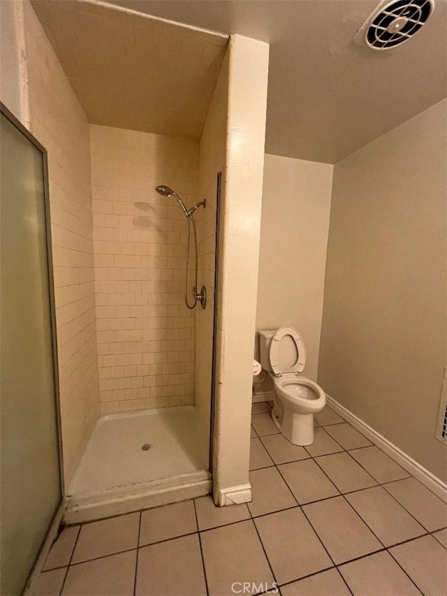 bathroom featuring toilet, tile patterned flooring, and tiled shower