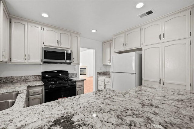 kitchen with sink, white cabinetry, light stone countertops, black gas range oven, and white refrigerator