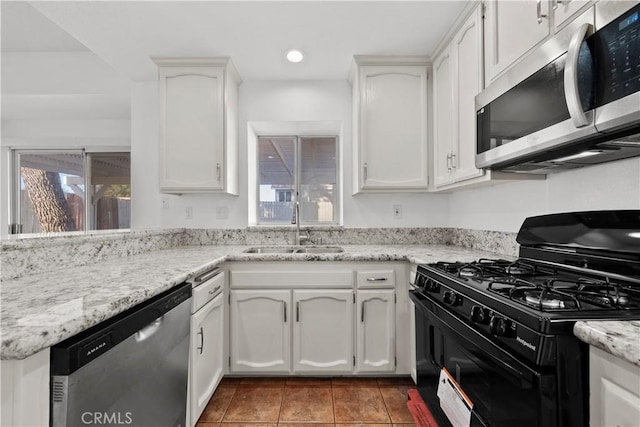 kitchen with light tile patterned floors, stainless steel appliances, white cabinets, light stone counters, and sink