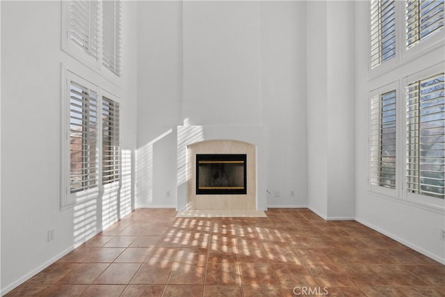 unfurnished living room with a towering ceiling, a tiled fireplace, and tile patterned flooring