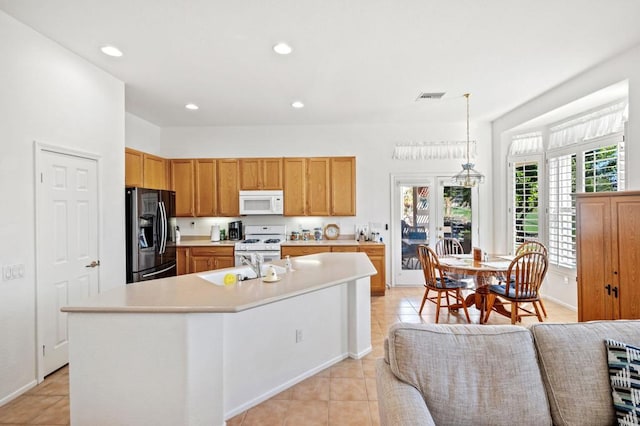 kitchen featuring white appliances, sink, hanging light fixtures, light tile patterned floors, and a center island with sink