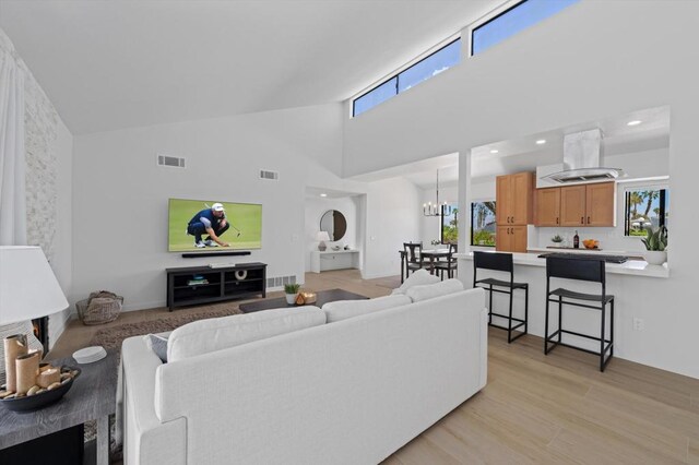 living room with an inviting chandelier, a wealth of natural light, light hardwood / wood-style floors, and high vaulted ceiling