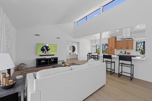 living room featuring high vaulted ceiling, a wealth of natural light, light hardwood / wood-style flooring, and an inviting chandelier