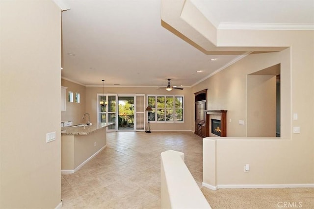 unfurnished living room with crown molding, baseboards, a glass covered fireplace, a ceiling fan, and a sink