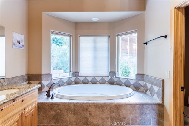 bathroom featuring a relaxing tiled tub, vanity, and a healthy amount of sunlight