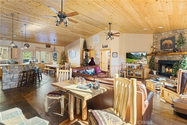 dining room with ceiling fan, wood ceiling, a stone fireplace, and high vaulted ceiling