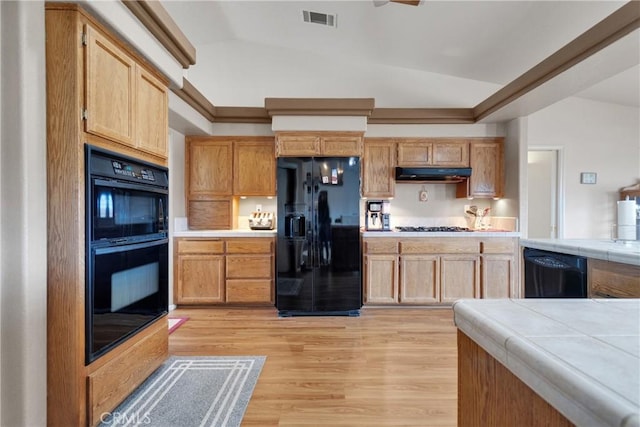 kitchen featuring tile counters, lofted ceiling, light hardwood / wood-style flooring, and black appliances