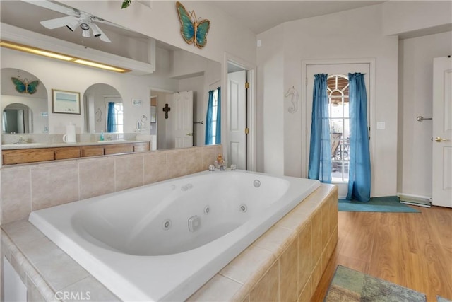 bathroom featuring tiled bath, sink, hardwood / wood-style floors, and ceiling fan