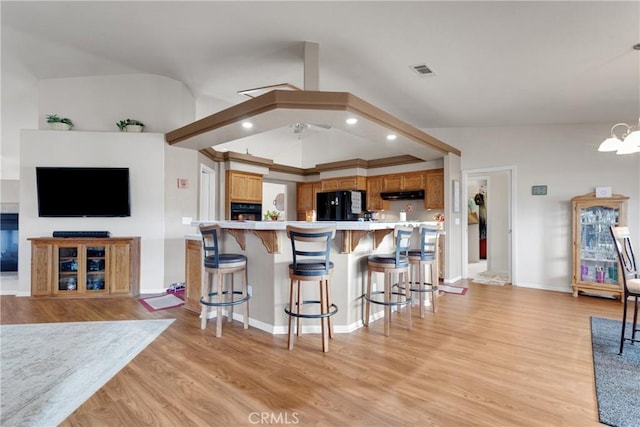 kitchen with light hardwood / wood-style floors, kitchen peninsula, black refrigerator, hanging light fixtures, and ceiling fan with notable chandelier