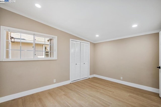 unfurnished bedroom featuring ornamental molding, light hardwood / wood-style flooring, vaulted ceiling, and a closet