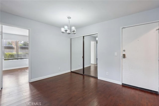 spare room with an inviting chandelier and dark hardwood / wood-style floors