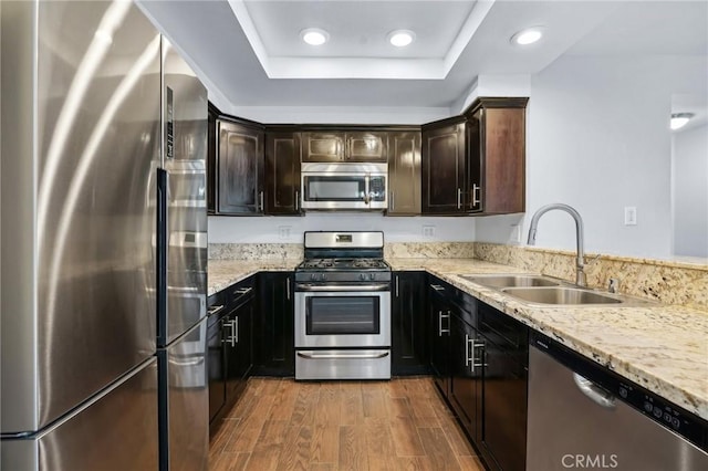 kitchen featuring dark brown cabinetry, sink, wood-type flooring, appliances with stainless steel finishes, and light stone countertops