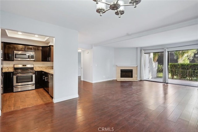 unfurnished living room featuring a raised ceiling, an inviting chandelier, and dark hardwood / wood-style flooring