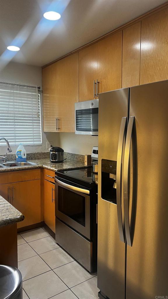 851 S Mollison Ave Unit 29, El Cajon, CA 92020 - kitchen featuring appliances with stainless steel finishes, light tile patterned floors, stone counters, and brown cabinetry
