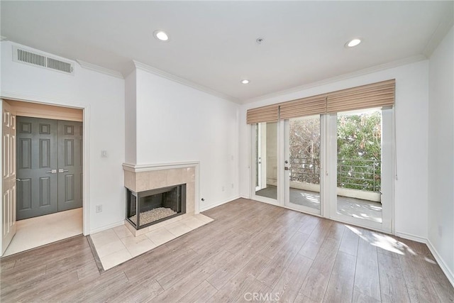 unfurnished living room featuring a tile fireplace, ornamental molding, and light hardwood / wood-style floors