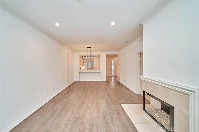 unfurnished living room with light wood-type flooring, an inviting chandelier, ornamental molding, and a tile fireplace