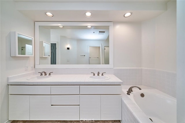 bathroom featuring tiled tub and vanity