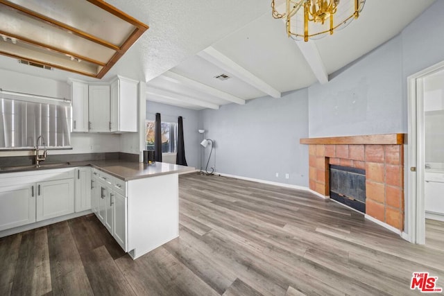 kitchen with white cabinetry, hardwood / wood-style floors, kitchen peninsula, a tiled fireplace, and sink